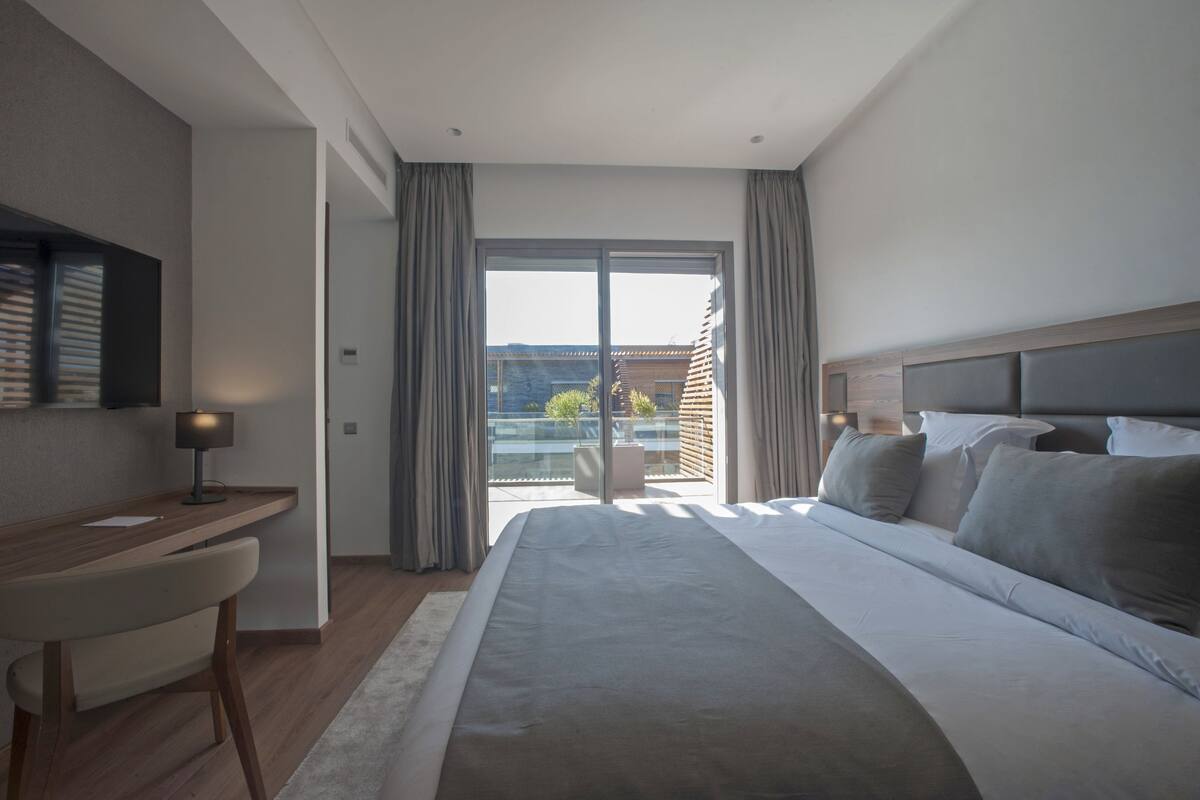 Une chambre d’hôtel moderne dotée d’un grand lit, d’un bureau et d’un balcon avec des rideaux.