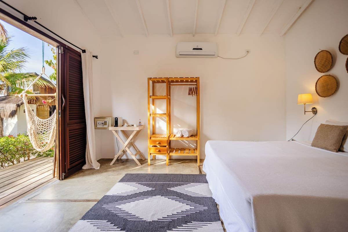 Ein Schlafzimmer mit Bett, Schreibtisch, Stuhl, einer Hängematte und Blick ins Freie.