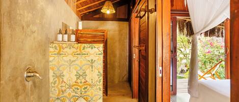 A narrow hallway with a tiled wall, a wooden door, and a bed with white bedding.