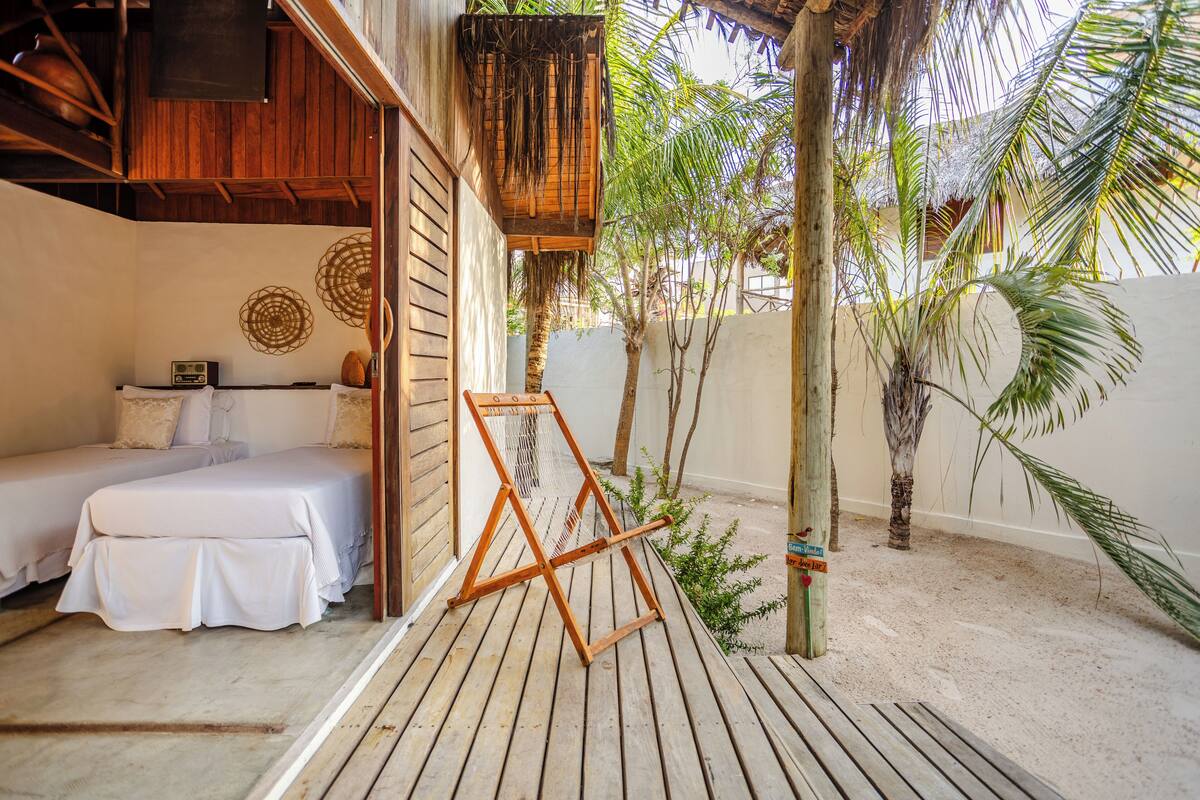 Ein Schlafzimmer mit Holzboden, einem Bett mit weißer Bettwäsche, einem hängenden Stuhl aus Bändern und einem kleinen Tisch mit einem Radio.