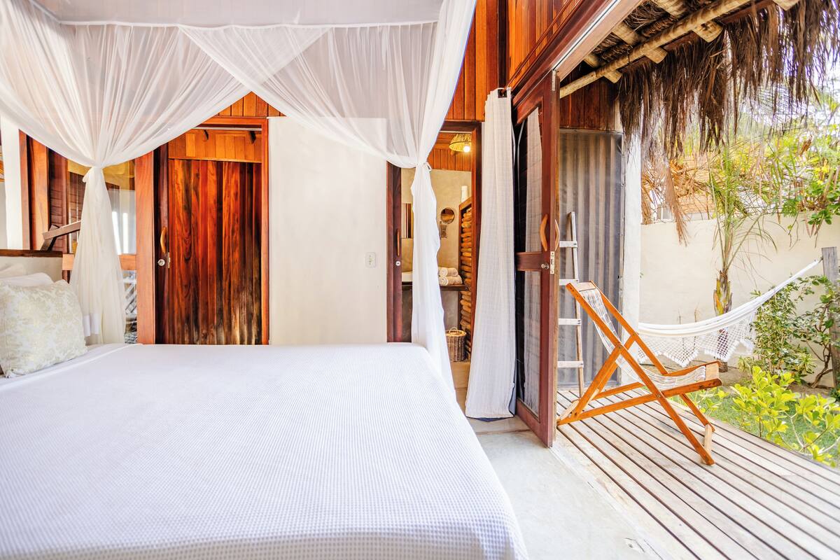 Ein Schlafzimmer mit einem großen Bett, einer Holztür, einer Hängematte und Blick auf einen Garten.