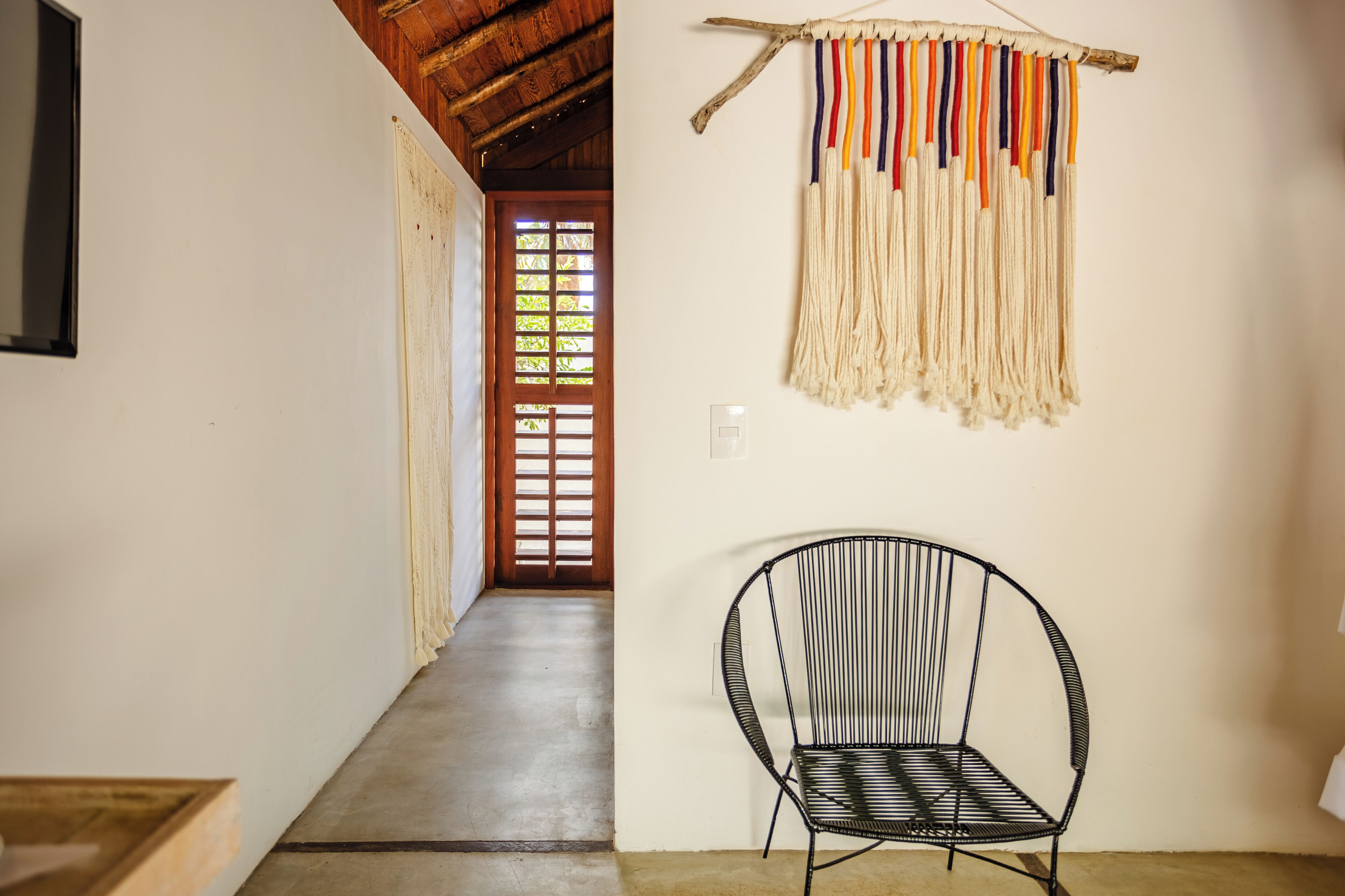 A hallway with a black metal chair, a wall-mounted macrame piece, and a wooden door with a window.