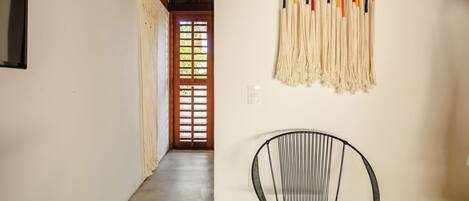 A hallway with a black metal chair, a wall-mounted macrame piece, and a wooden door with a window.
