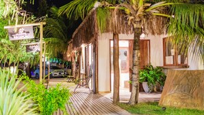 Una estructura con techo de paja con un letrero que dice "LA COZINHA", rodeada de exuberante follaje y una terraza de madera.