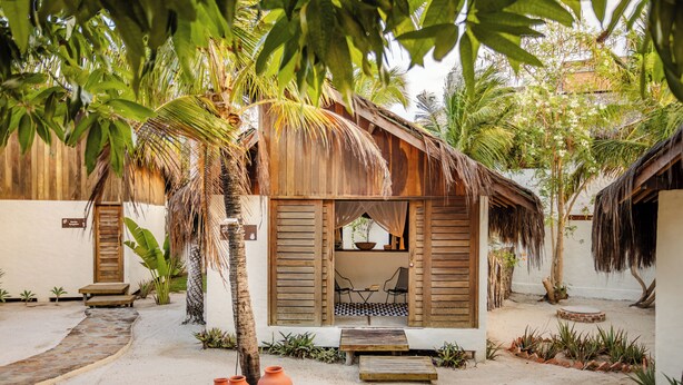 Un resort tropical con cabañas de madera, una estructura de techo de paja y un sendero de arena.