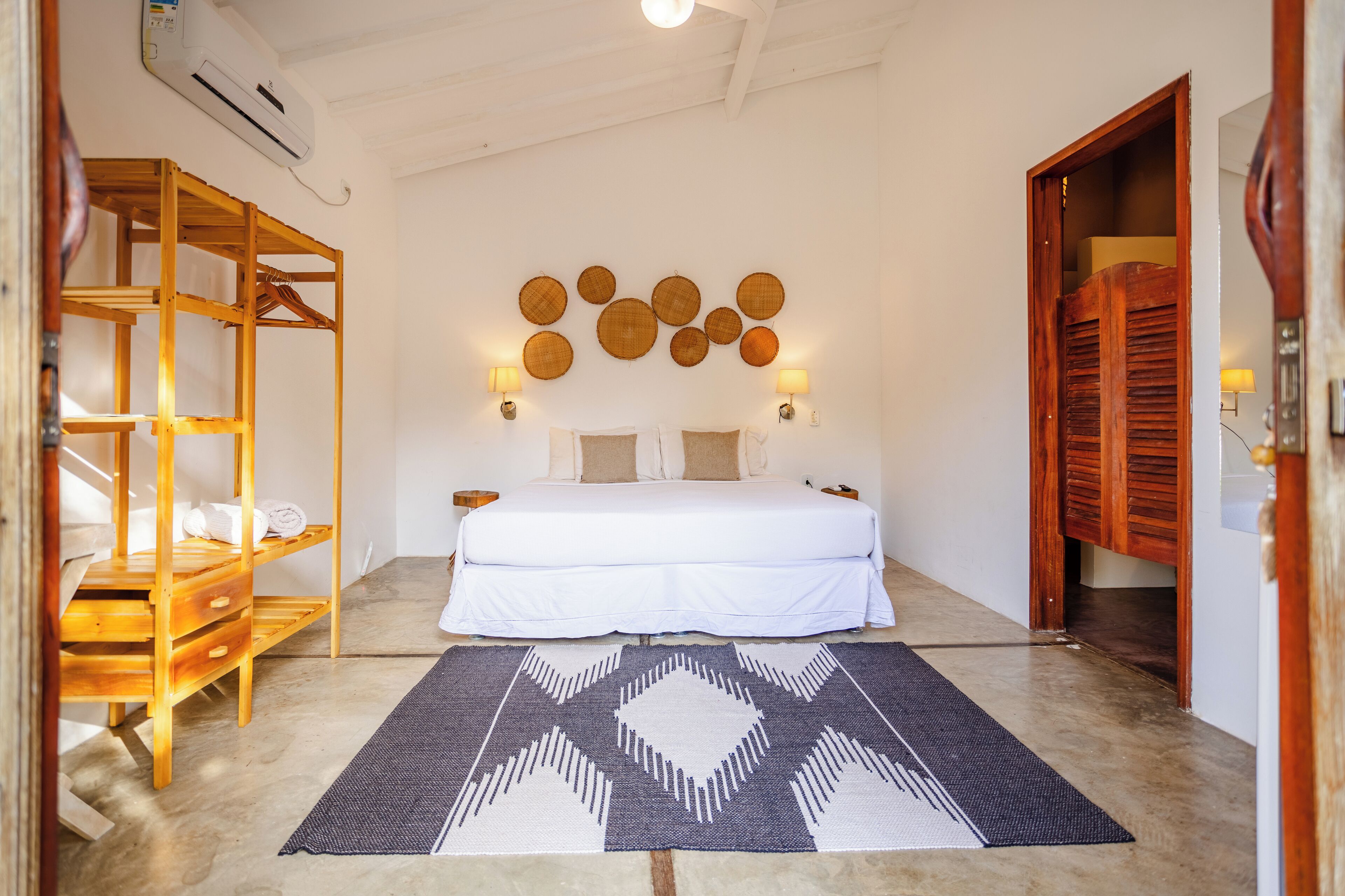 A bedroom with a bed, wooden wardrobe, wall-mounted lamps, and a patterned rug.