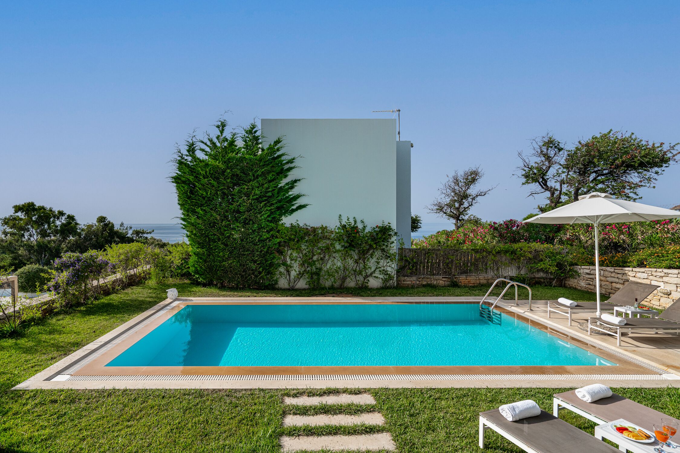 A rectangular swimming pool with a clear blue water, surrounded by a well-maintained lawn and a stone wall.