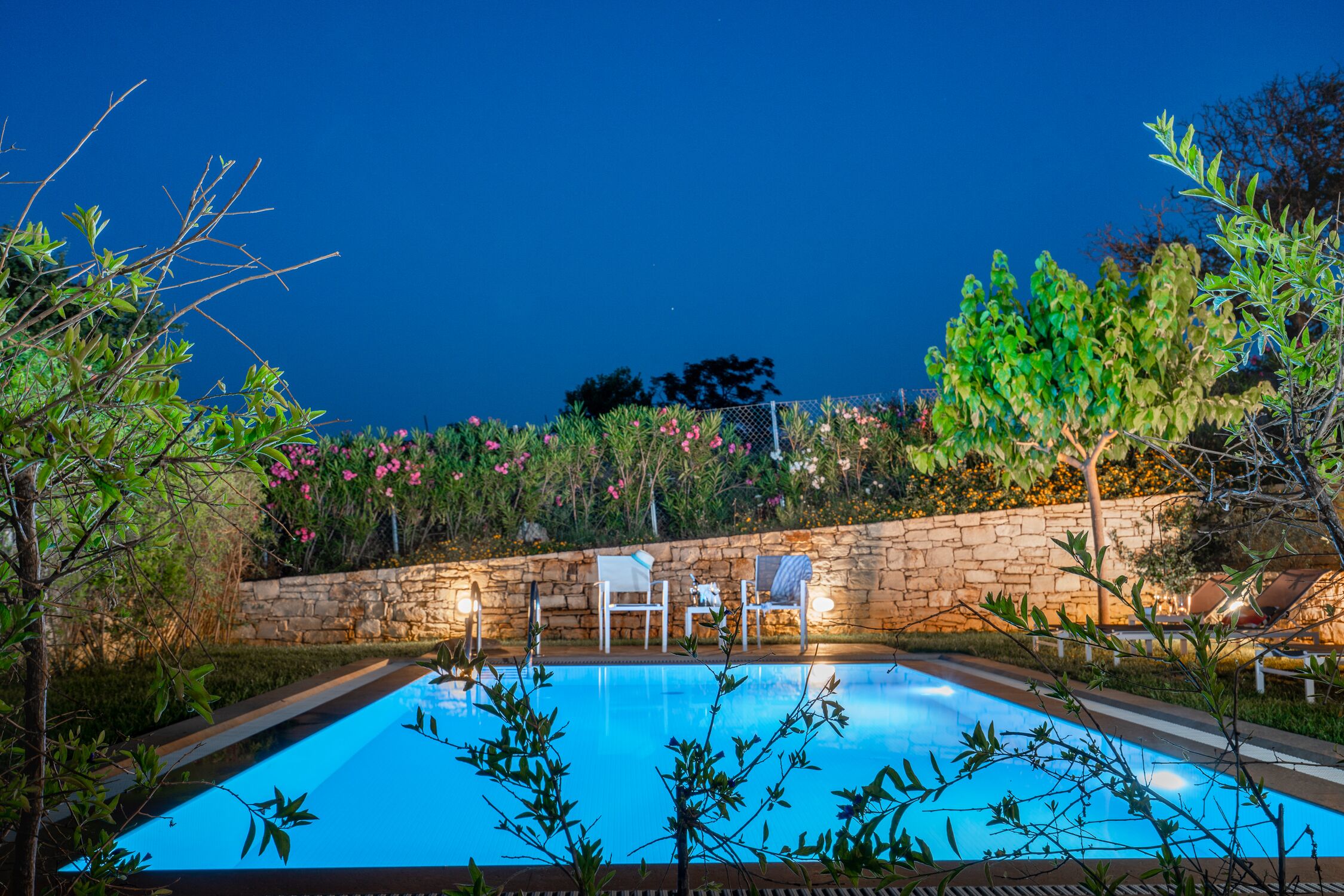 A swimming pool with a stone wall and chairs.