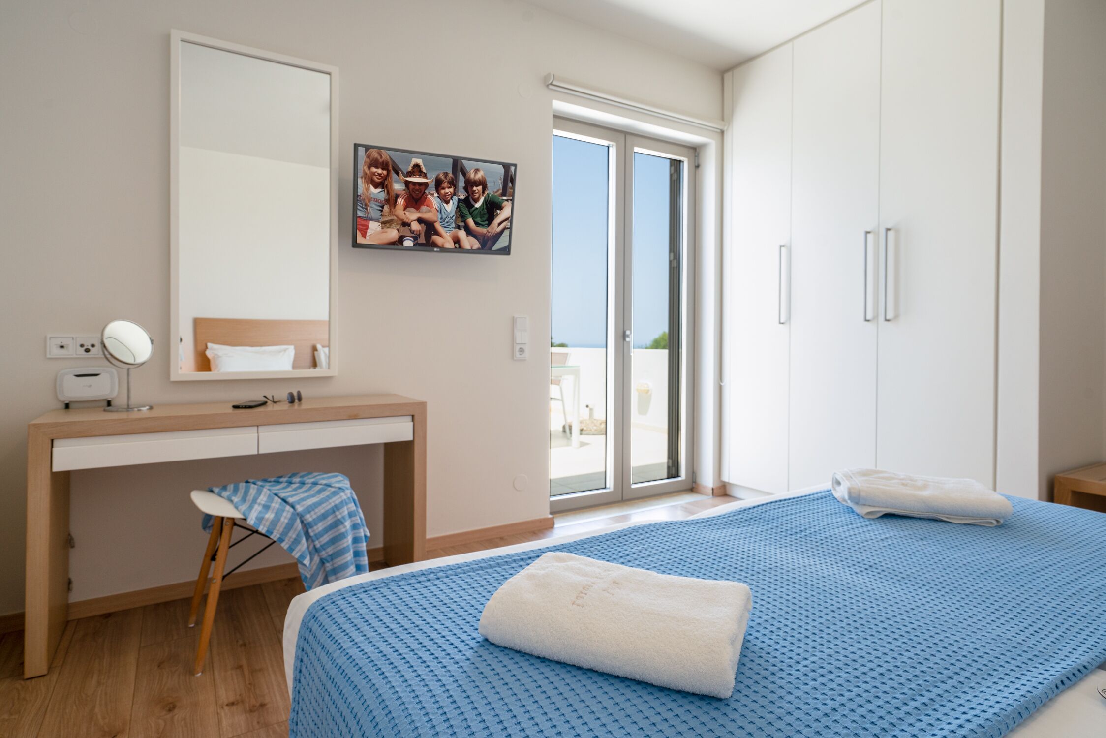 A bedroom with a bed, a desk, a chair, a mirror, and a window with a view.