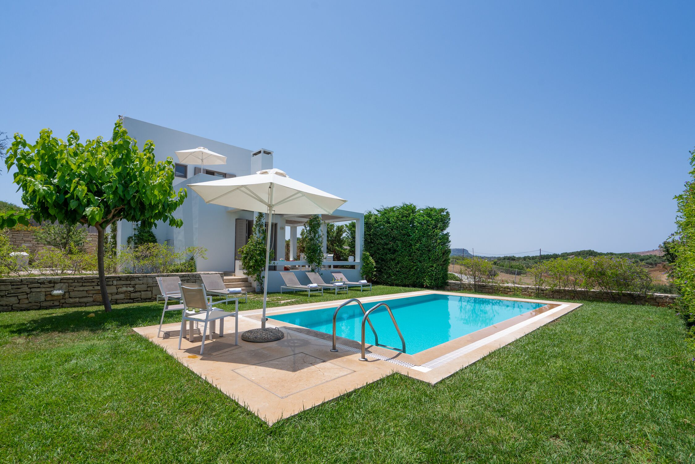 Une maison moderne dotée d’une piscine, d’un espace salon extérieur et d’un mur en pierre.