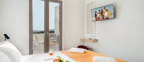 A hotel room with a bed, a tray with fruit and juice, a TV on the wall, and a balcony with a glass door.