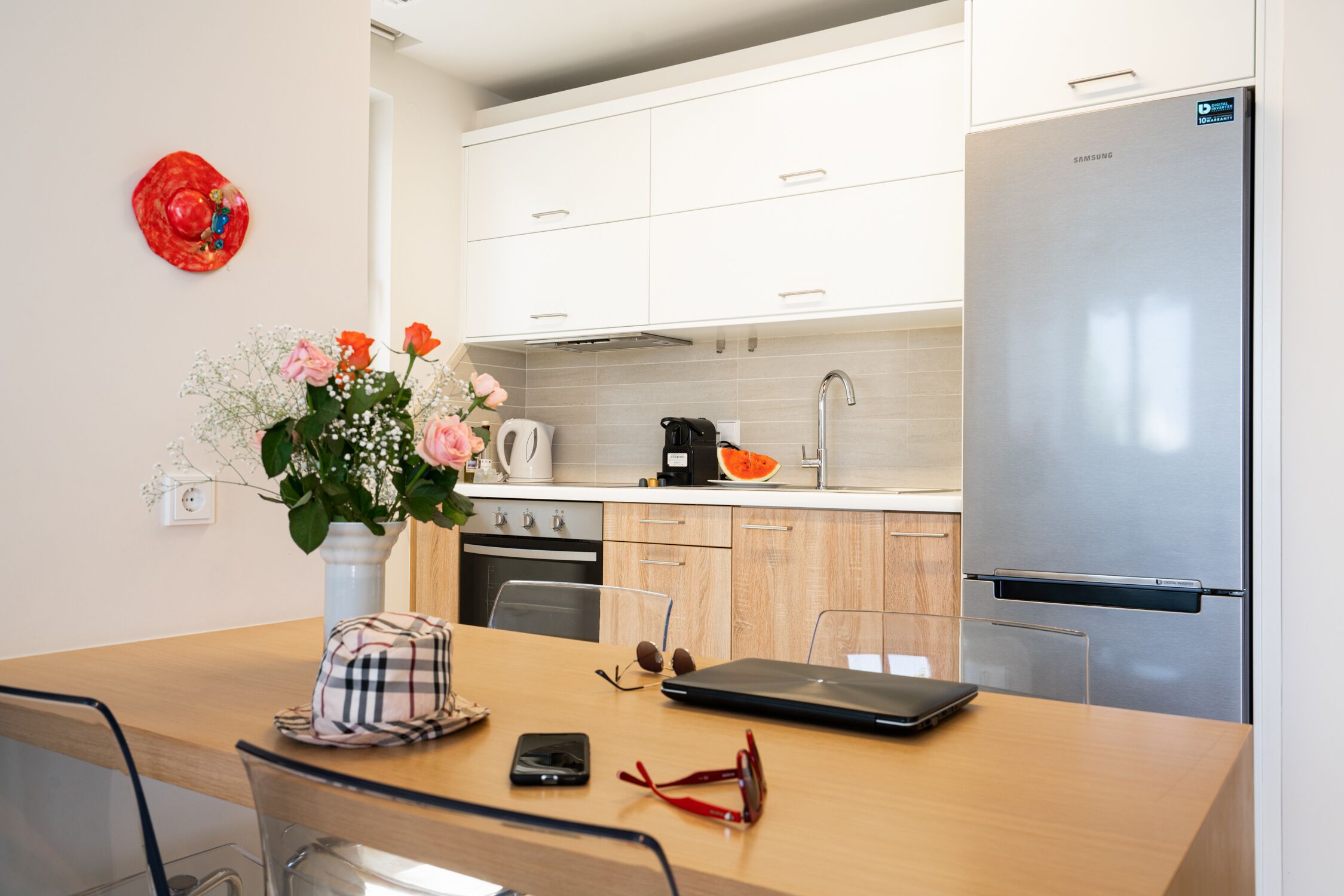 A modern kitchen with white cabinets, a stainless steel refrigerator, and a dining area with a wooden table.