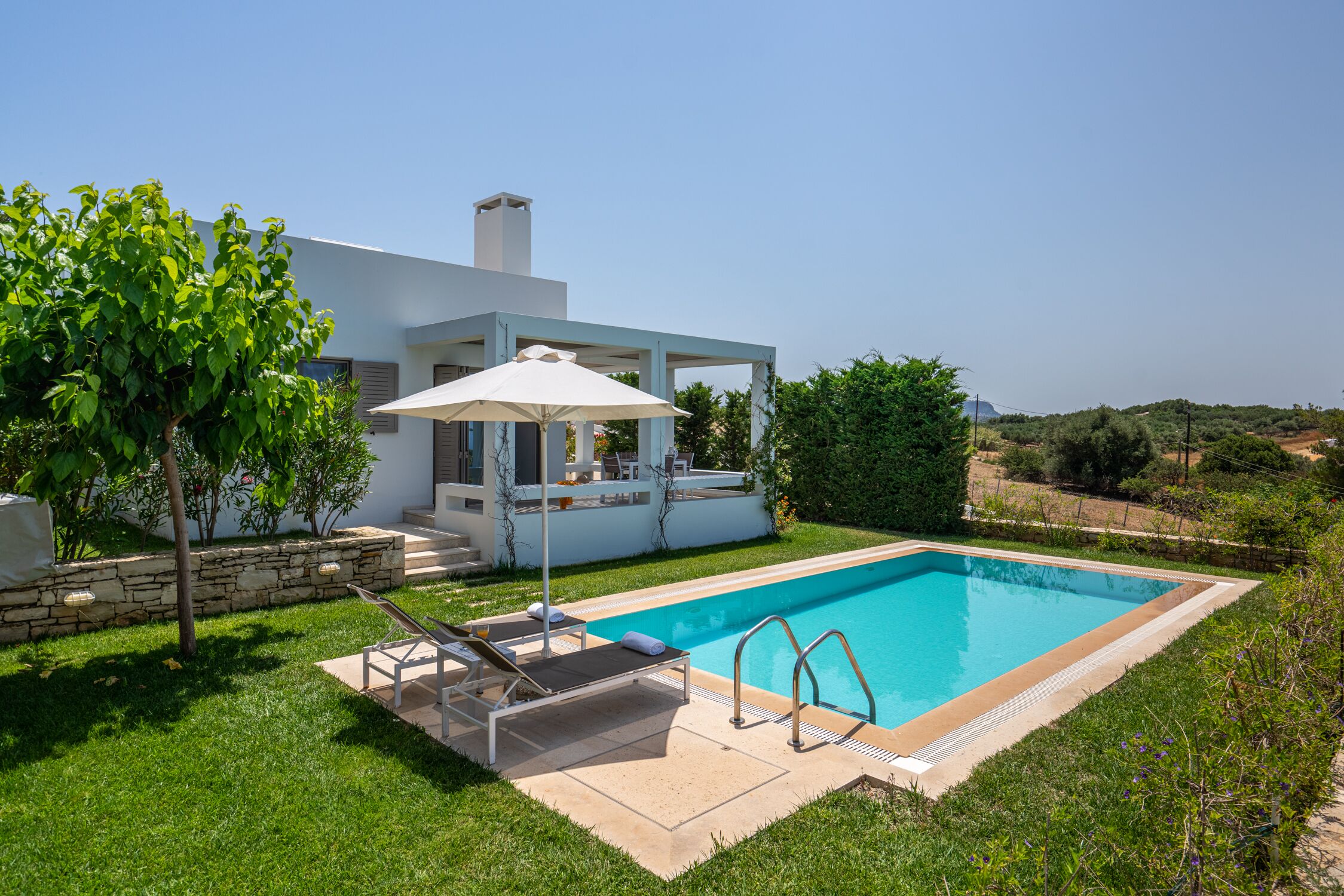 A modern house with a swimming pool, a covered patio, and a stone retaining wall.