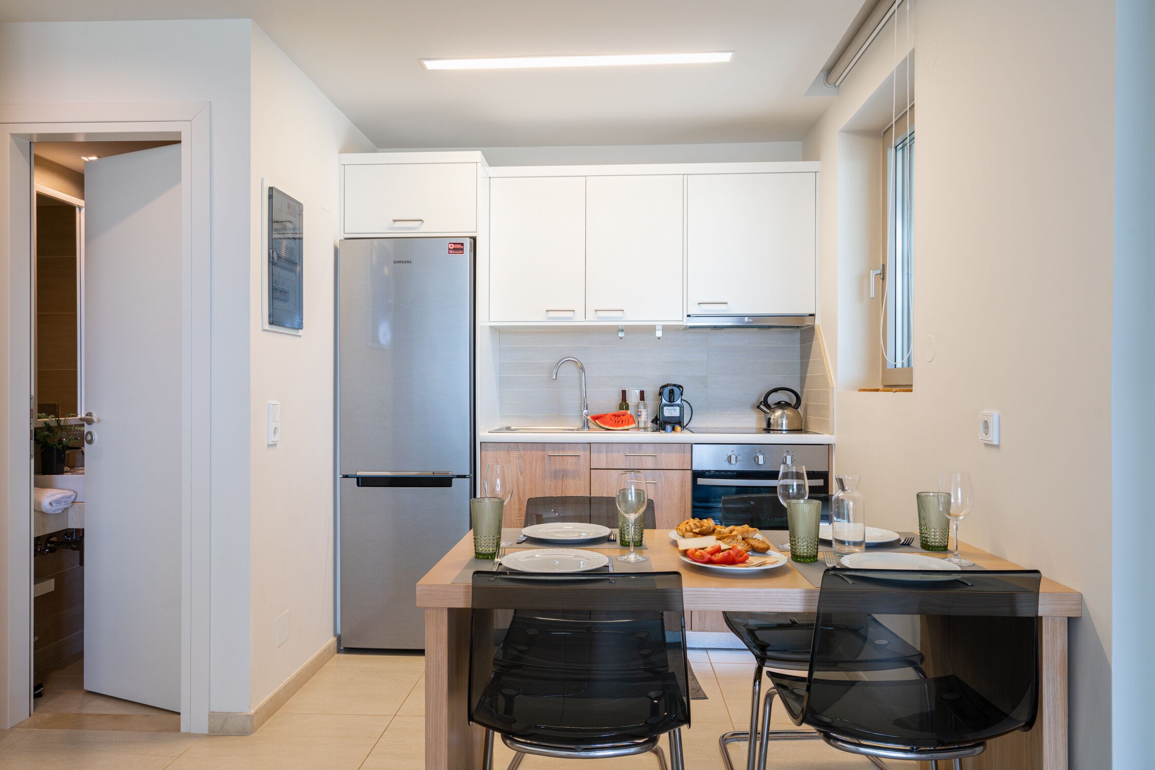 A modern kitchen with white cabinets, a stainless steel refrigerator, and a dining table set for four.