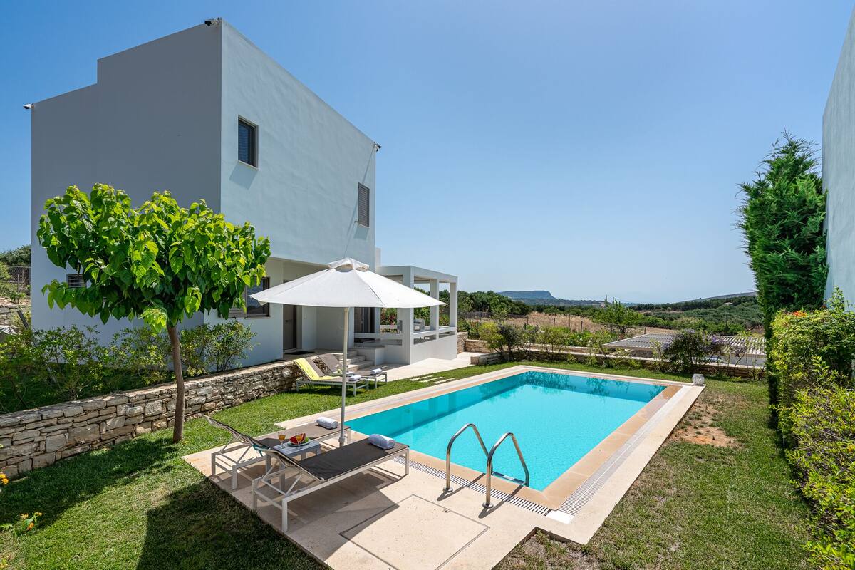 A modern house with a swimming pool, a stone wall, and a tree.