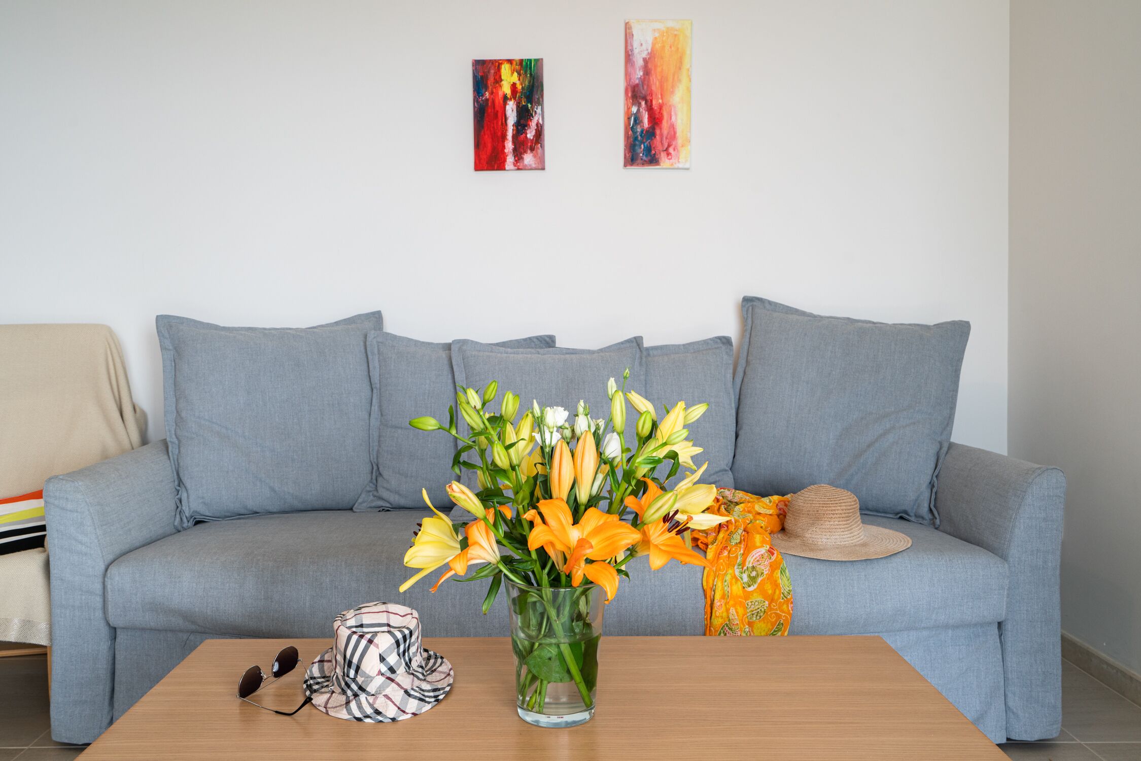 A living room with a grey sofa, a coffee table with a vase of flowers, and two abstract paintings on the wall.