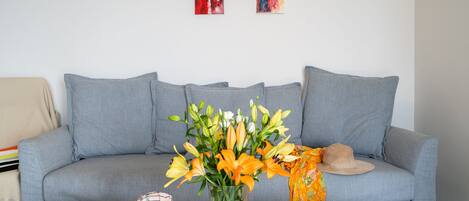 A living room with a grey sofa, a coffee table with a vase of flowers, and two abstract paintings on the wall.