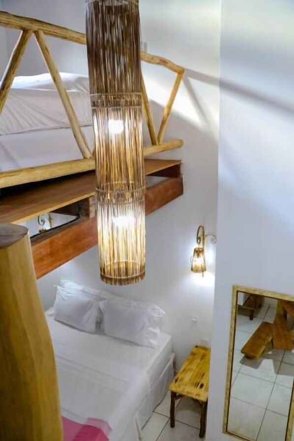 Un dormitorio con una cama, un banco de madera, una lámpara colgante y un espejo montado en la pared.