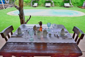A wooden table set for dining with a view of a swimming pool and lounge chairs in the background.