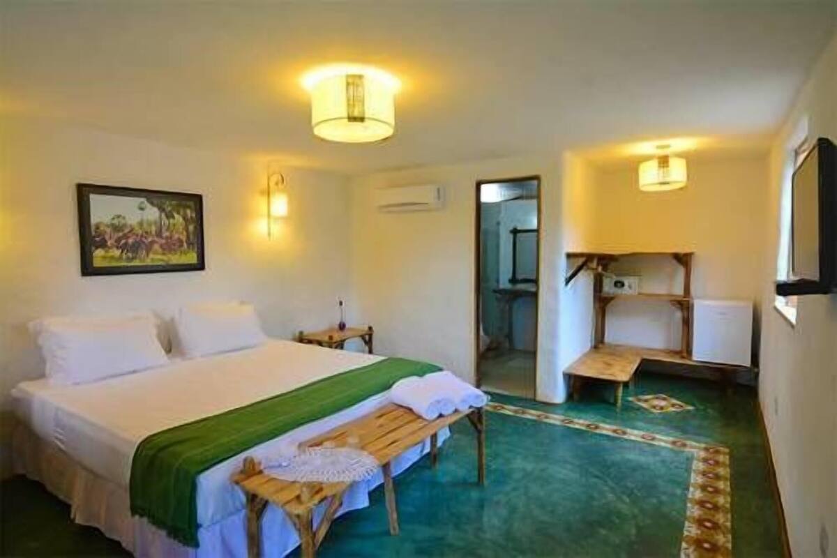 A hotel room with a bed, a bench, a painting, and a small table.