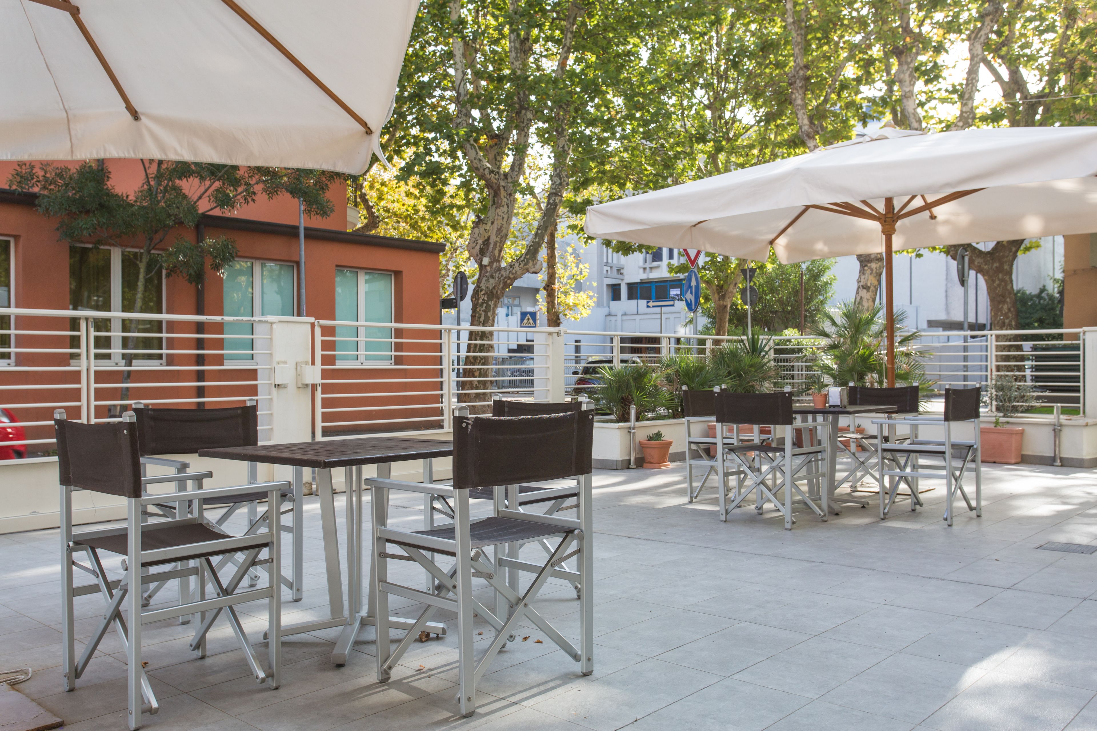 An outdoor patio with metal tables and chairs, umbrellas, and potted plants.