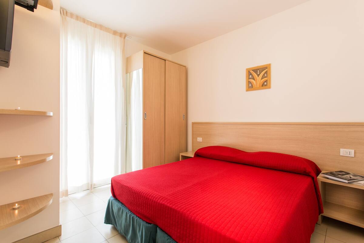 A hotel room with a bed, a wardrobe, a bedside table, and a wall-mounted artwork.