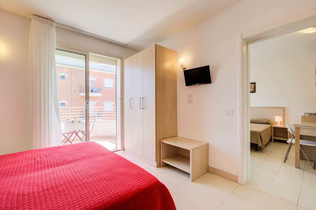 A modern hotel room with a bed, a TV, a desk, and a balcony.