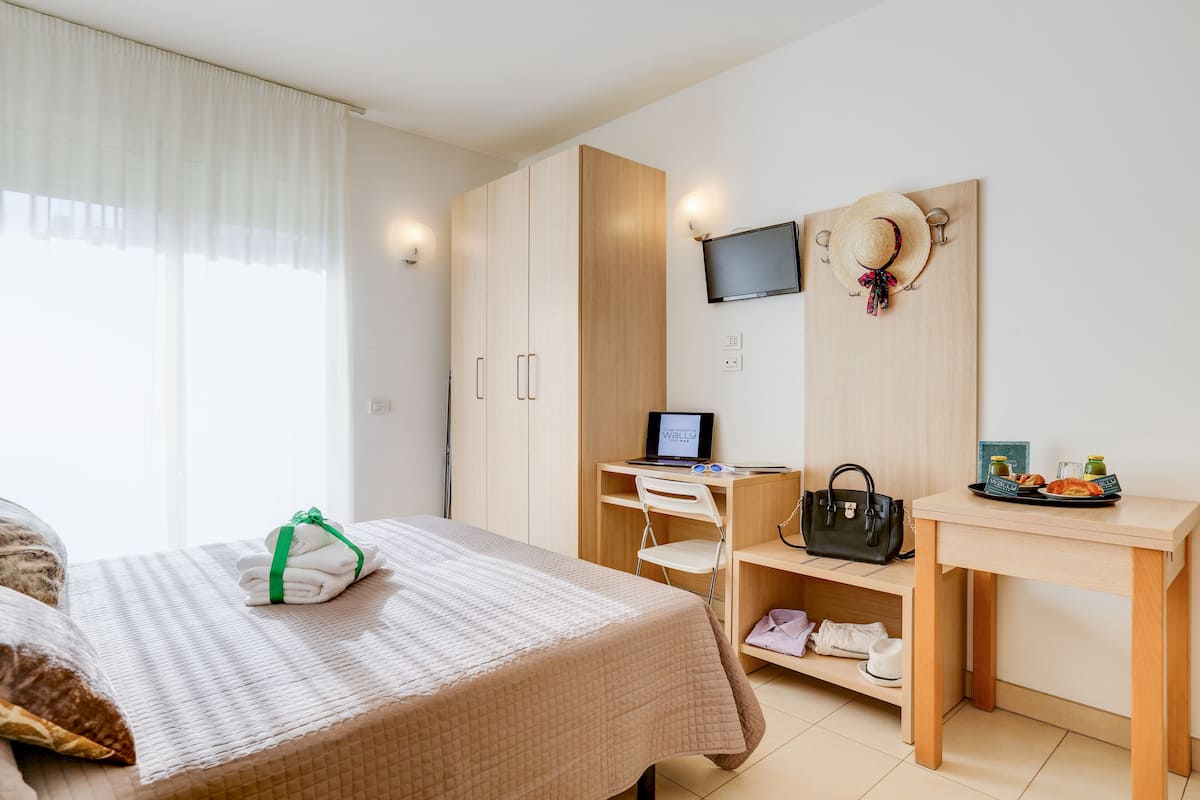 A hotel room with a bed, a desk with a computer, a TV, and a wall-mounted hat decoration.