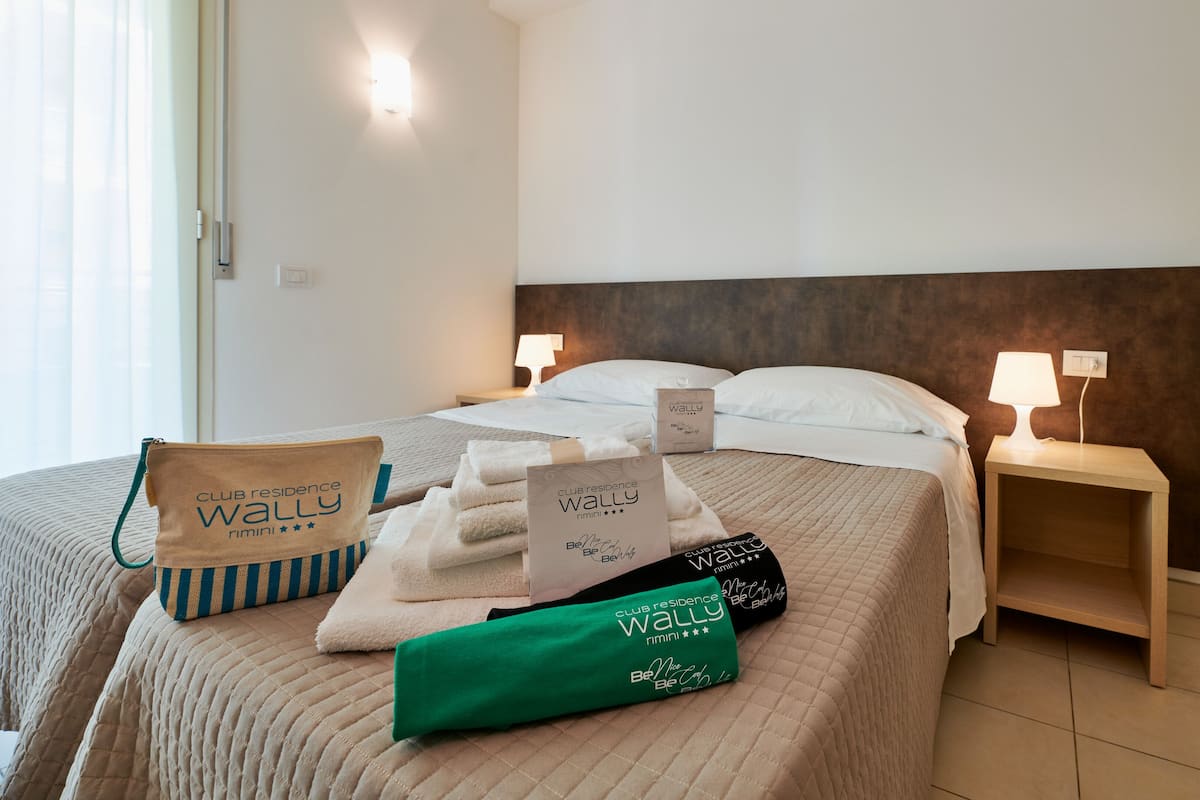 A hotel room with a bed, two bedside tables, a nightstand, and a window with curtains.