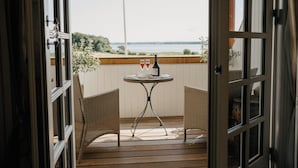 An open door leading to a balcony with wicker chairs, a small round table, and a bottle and glasses on the table. - Jungshoved Præstegård (Praesto)