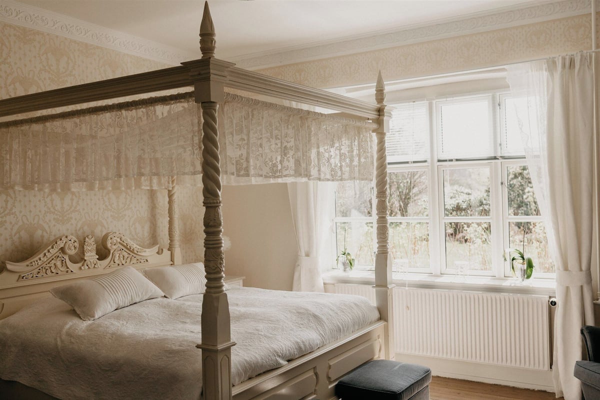 A four-poster bed with a white canopy, a window with white curtains, and a radiator below.