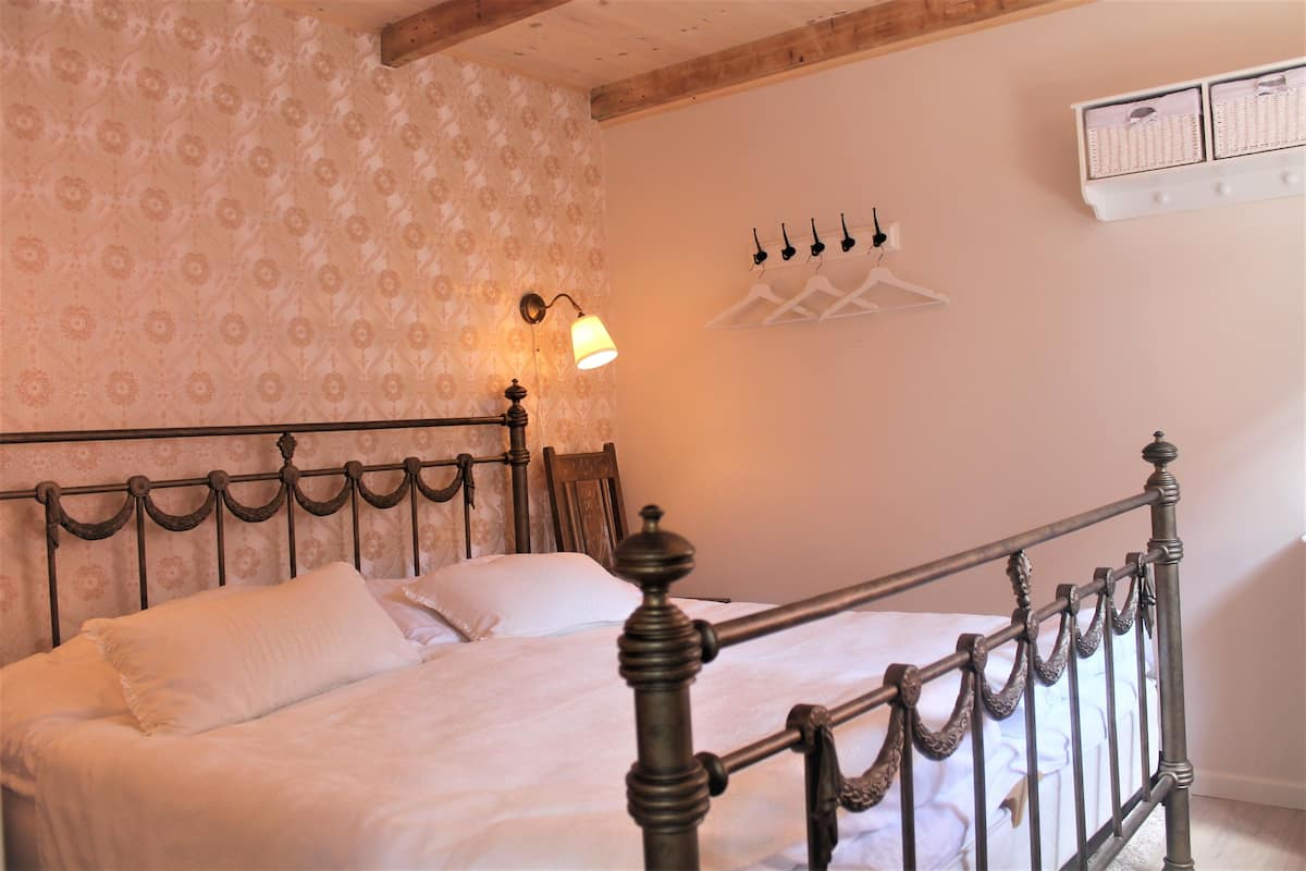 A neatly made bed with a headboard, a wall-mounted light, and a white storage unit with hangers.
