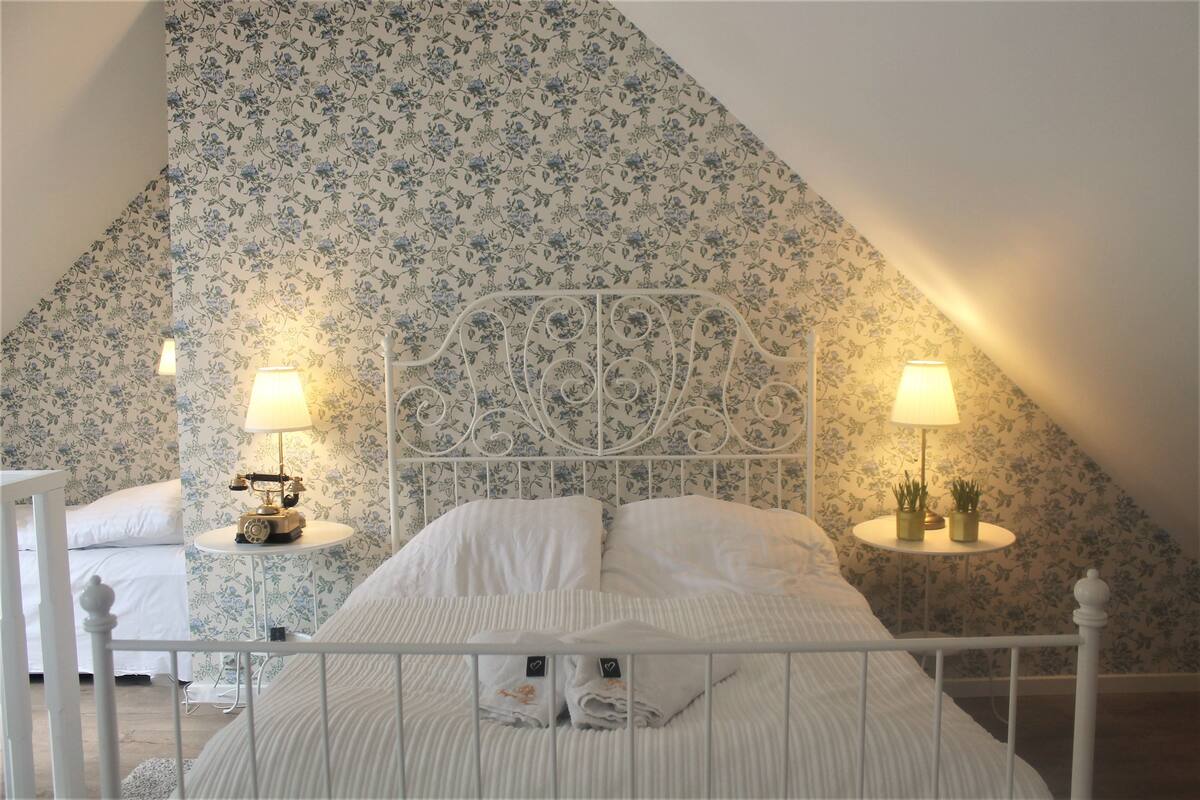 A bedroom with a white bed, floral wallpaper, and two bedside tables with lamps.
