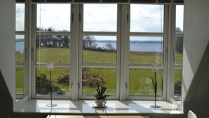 A room with large windows overlooking a grassy landscape and a body of water. - Jungshoved Præstegård (Praesto)