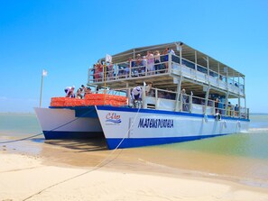 A ferry with multiple decks and passengers, docked at a beach.