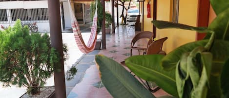 Un espacio al aire libre techado con una hamaca, sillas y plantas en macetas.