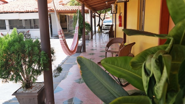 A covered outdoor area with a hammock, chairs, and potted plants.