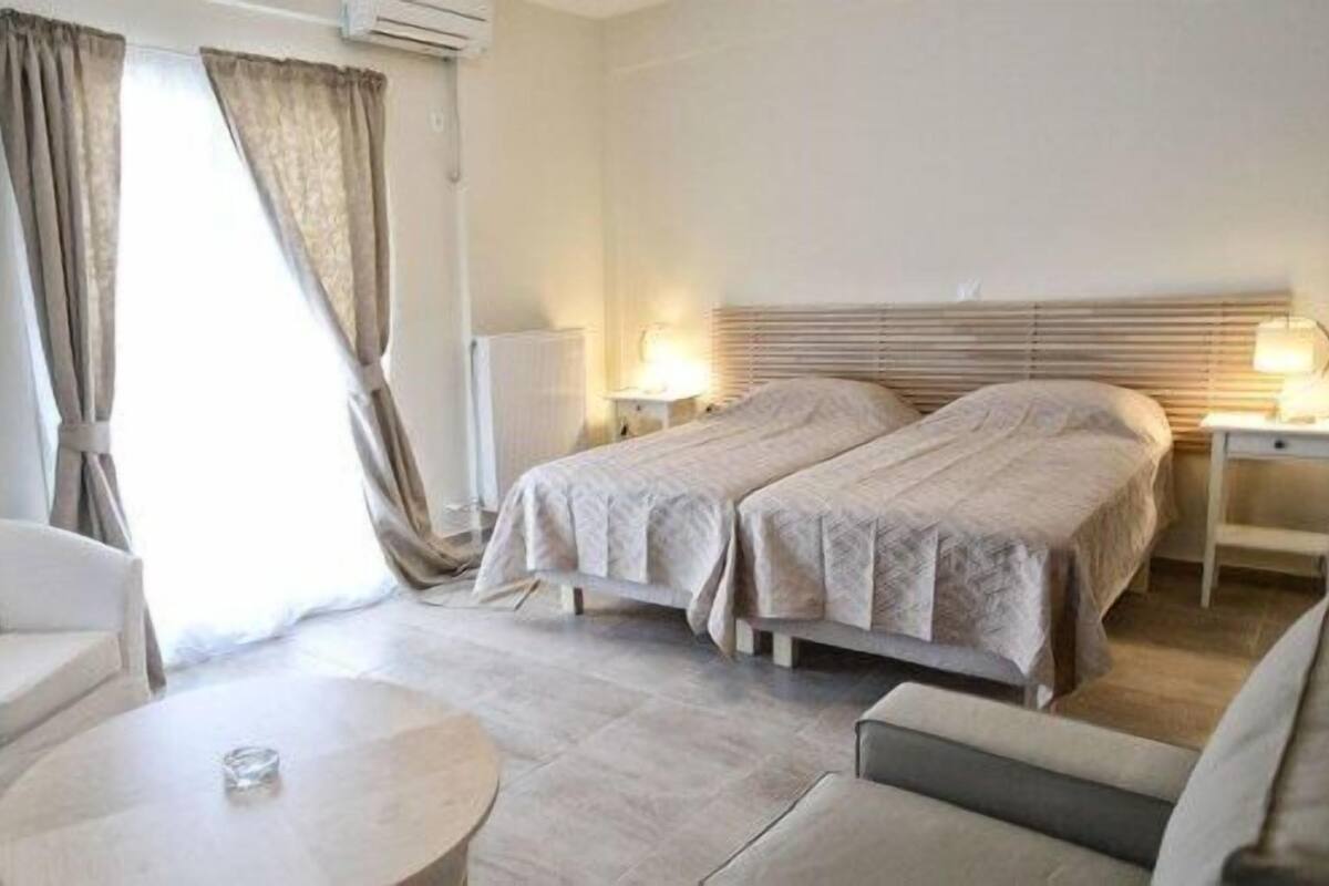 A hotel room with a bed, two bedside tables, a chair, a small round table, and a fireplace.