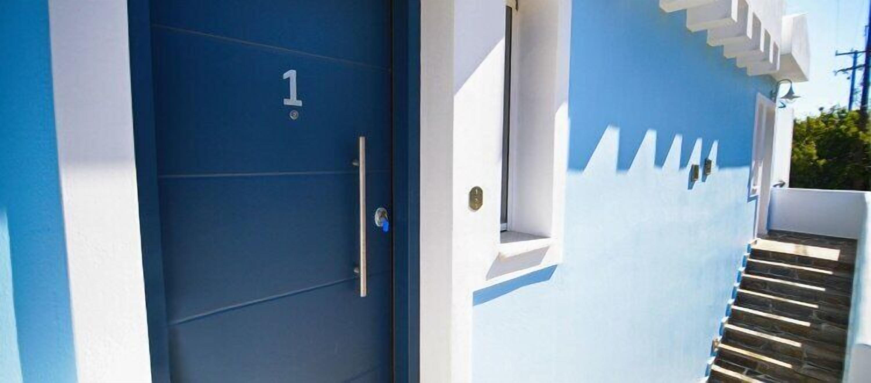 A blue door with a number '1' sign, white exterior walls, and a staircase leading to a balcony.