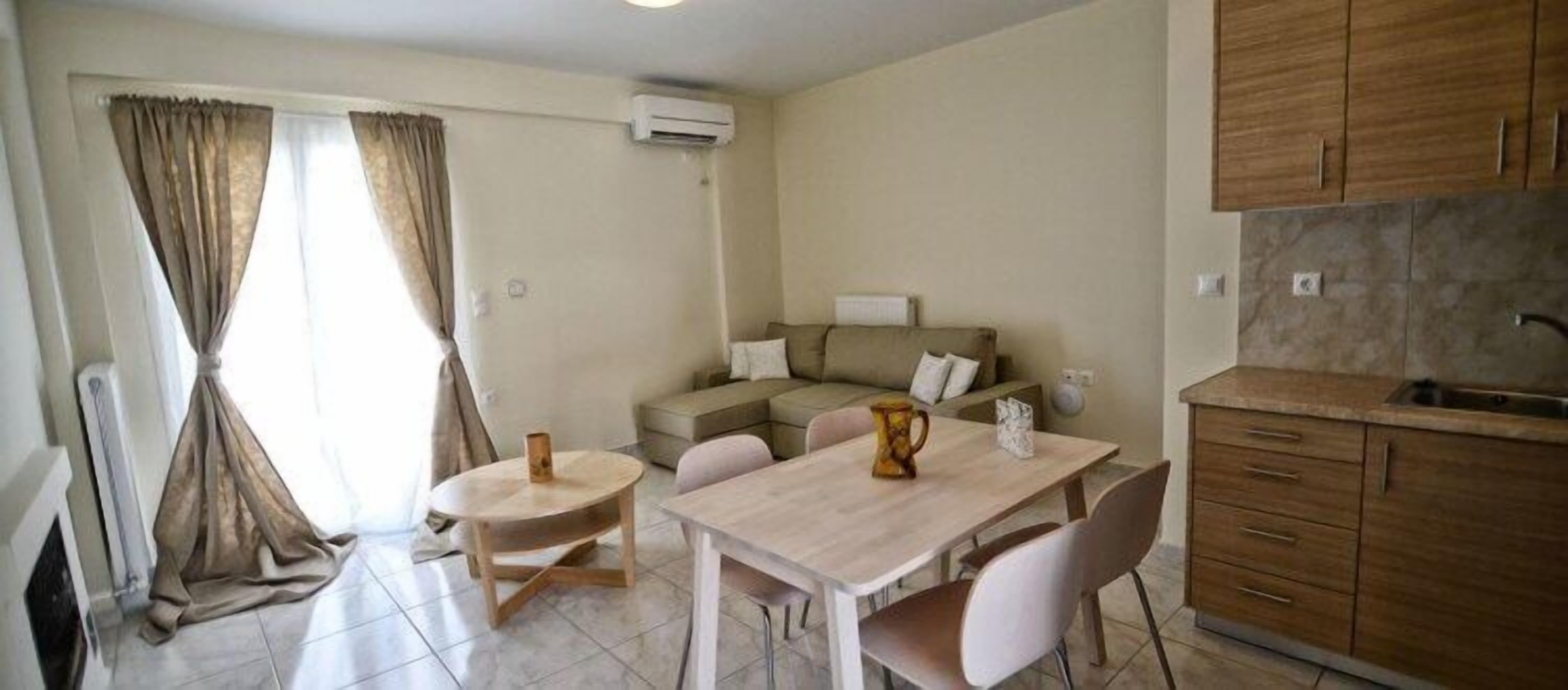 Un espacio habitable compacto con comedor, sofá, cocina con armarios de madera y ventana con cortinas.