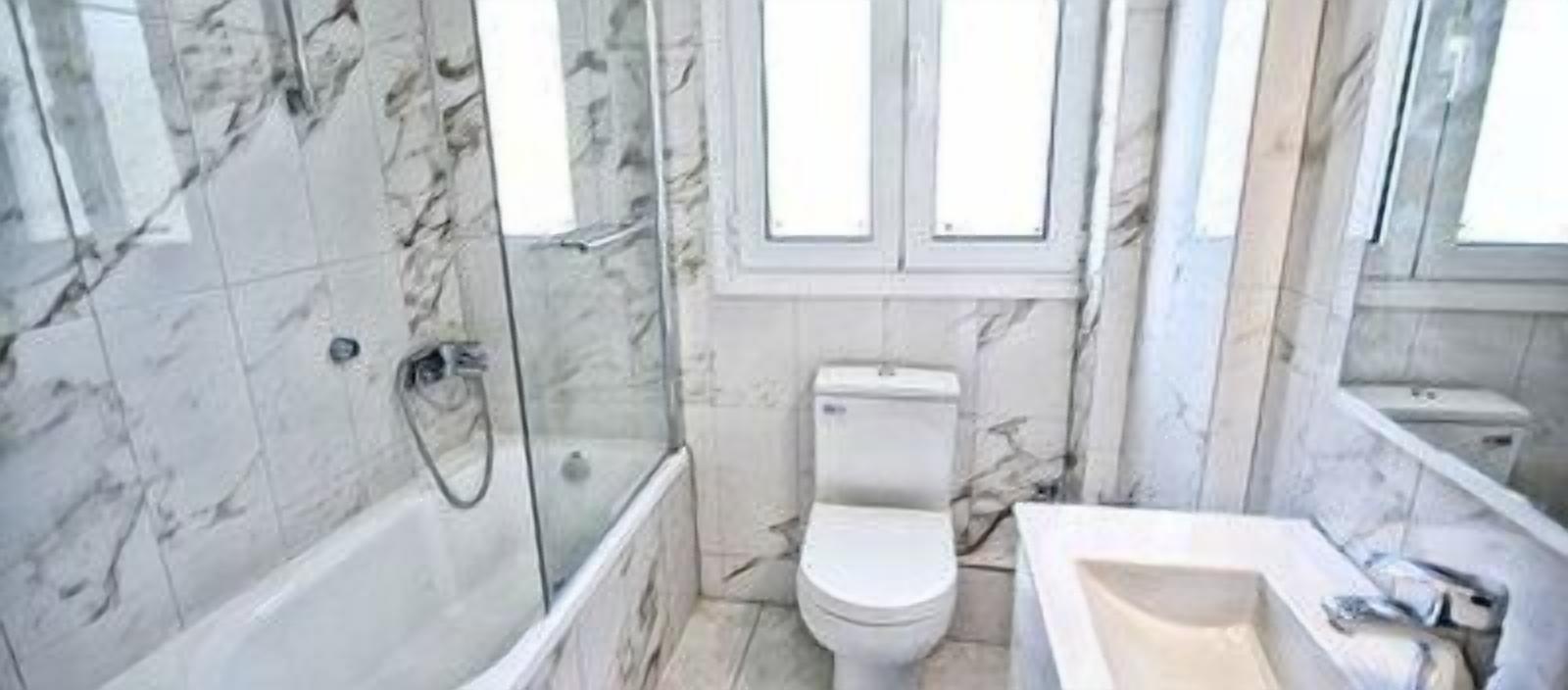 A bathroom with a marble floor, a bathtub, a toilet, and a sink.