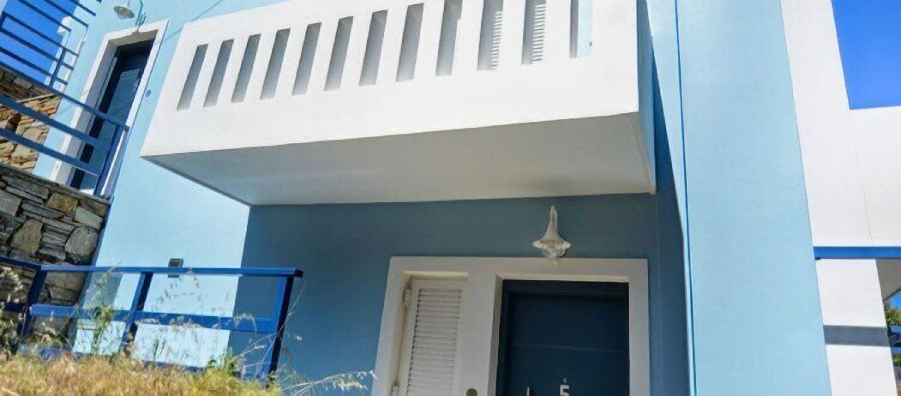 A modern building with a blue facade, a white door, and a small balcony with a railing.