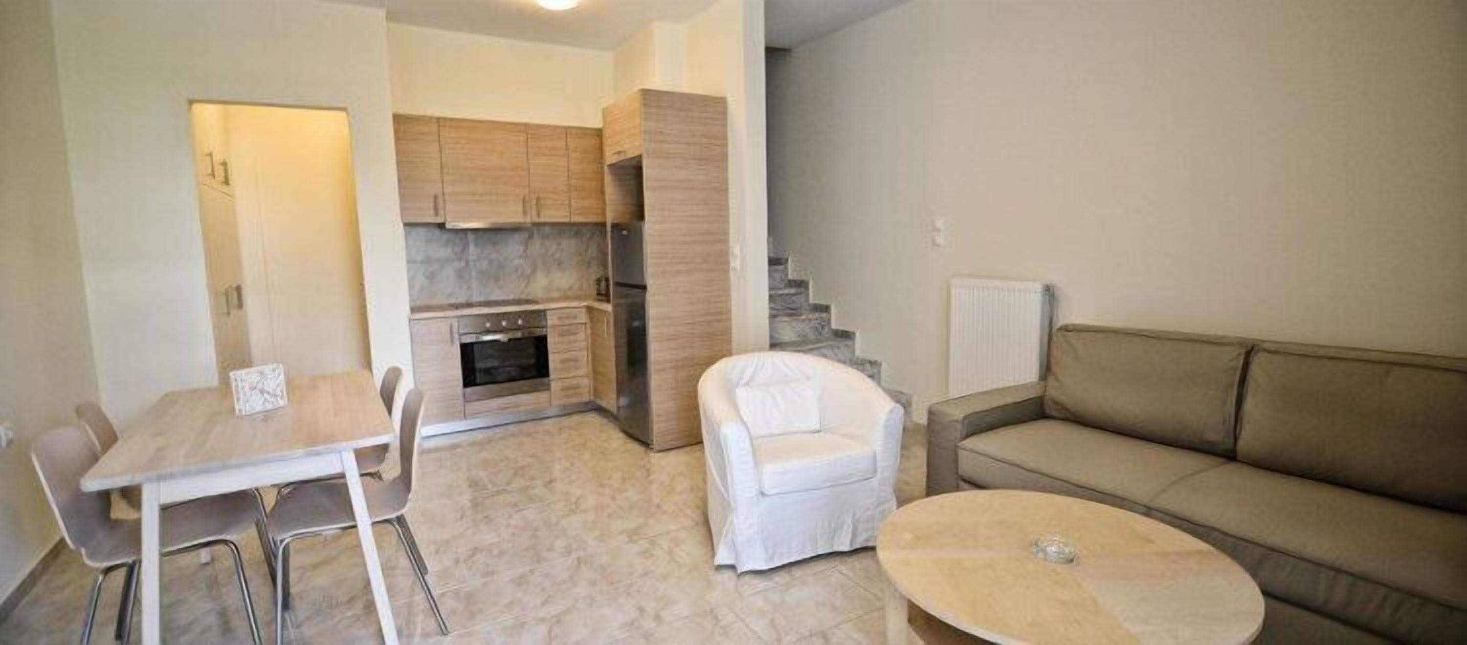 Un espace de vie compact comprenant un coin repas, une kitchenette, une chaise blanche, un canapé et un escalier.