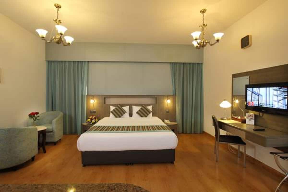 A hotel room with a large bed, a desk with a chair, a television, and two bedside lamps.