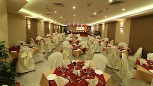 A banquet hall with round tables set for dining, white chairs, and a stage at the front. - Florida City Hotel Apartments (Dubai)