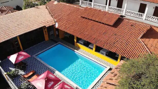 A swimming pool with a tiled deck, surrounded by umbrellas and a wooden deck. - Hotel Pousada dos Ventos (Parnaíba)