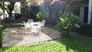 A patio with a table and chairs, surrounded by greenery and a building in the background. - Hotel Pousada dos Ventos (Parnaíba)