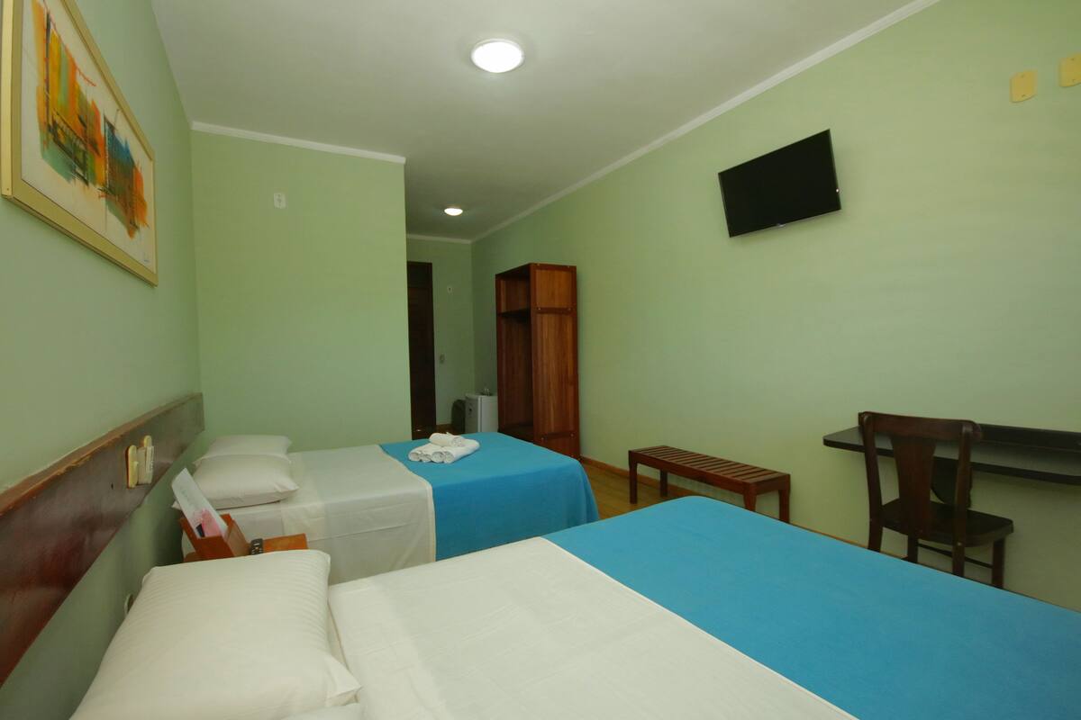 A hotel room with two beds, a television, a wooden chair, and a small table.