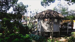A rustic wooden structure with a thatched roof, surrounded by lush greenery and a wooden deck. - Hotel Pousada dos Ventos (Parnaíba)