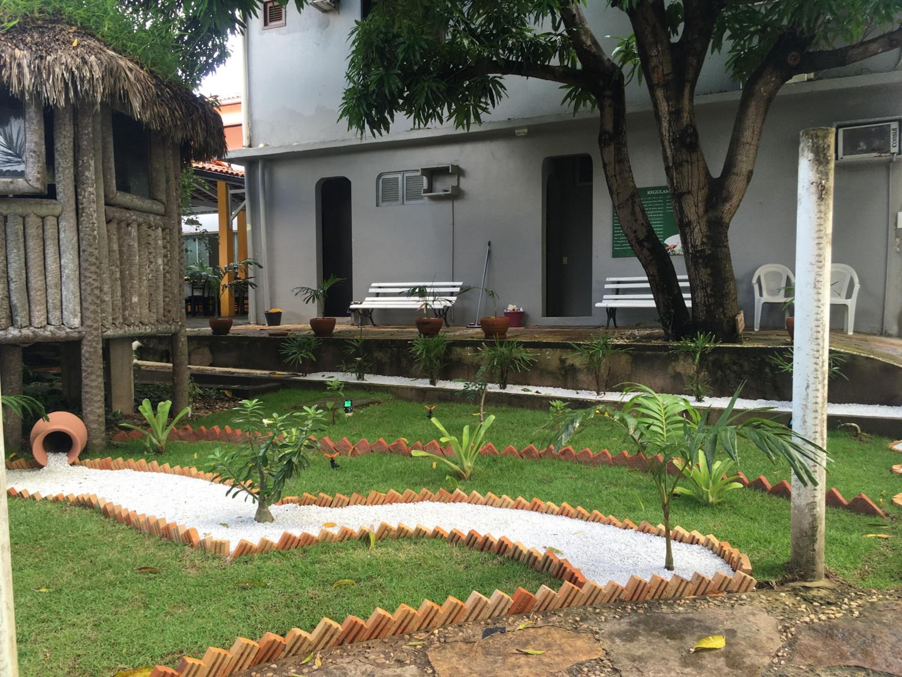 Um pátio com uma construção de telhado de palha, plantas em vasos e um banco branco.